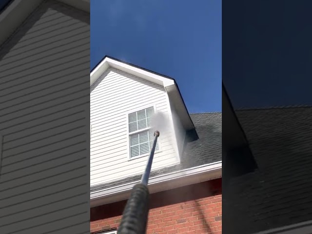 Washing the dormers of a white vinyl house using a pressure washer.