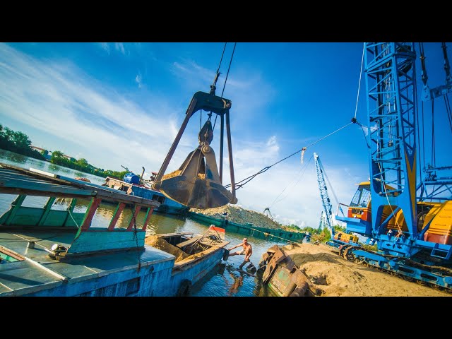 Crawler Cranes shovel sand and rocks into small boats on the river - GIANT IRON ARM